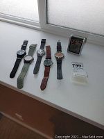 All five watches and the AcuRite monitor lined up on a white surface by a window