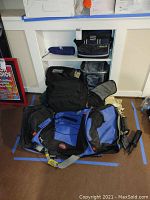 Wide view showing piled camping gear including backpacks and cooler bags, showing size and condition