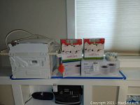Frigidaire air conditioning unit placed horizontally with power cord, two boxes of white satin globe lights and Levoit HEPA air filter box on a table near window.