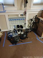 Wide view of the lot showing walking poles, snowboarding boots, helmet, air pump, and bottled water in background