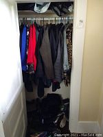 Full closet view showing multiple jackets and coats on hangers and shoes and accessories on the floor.