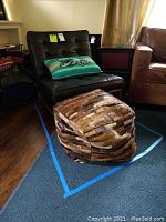 Overall view of black leather chair, patchwork ottoman, and decorative pillow on blue rug