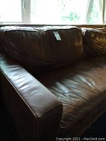 Close side view of the brown leather sofa showing the armrest and seat cushion with visible creasing and wear marks.