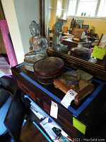 Buddha statue sitting on a wooden surface next to an oval woven jewelry box with a lid, with a mirror reflecting the statue.