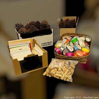 Photo showing boxes of envelopes, pine cones, a basket of multi-colored ribbon rolls, and a bag of wine corks.