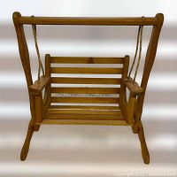 Front view of miniature wooden porch swing showing wooden slatted seat and backrest, rope suspension, and armrests.
