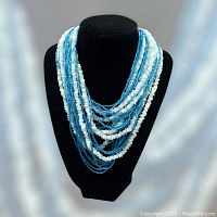 Front view of the multi-strand puka shell and blue glass beads choker on black necklace display stand.