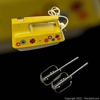 Yellow vintage Kenmore hand mixer with floral decals and two metal beaters isolated on black background.