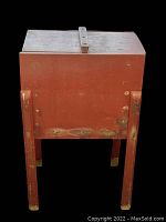 Front view of the vintage butter churn showing reddish-brown painted wooden structure and worn legs.