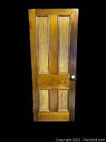 Front view of vintage wooden door showing four recessed panels and white porcelain knob on right side, varnished wood with warm honey tone.