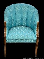 Front view of vintage mid-century modern tub chair showing fluted back, floral blue fabric, and detailed wooden trim on arms and legs.