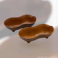 Pair of vintage peanut-shaped footed nut dishes shown together on a light background, highlighting the shape and color.