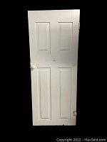 Full view of the white painted vintage wooden door showing four recessed panels and one porcelain doorknob.