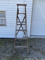 Front view of vintage wooden ladder showing five steps plus top platform, weathered wood with aged patina.