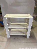 Front view of the white wooden 3-tiered shelf stand showing its structure and three shelves with slats.