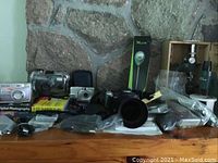 Overview of lot showing cameras, Digital Photography for Dummies book, microscope in wooden case, and various camera accessories arranged on a wooden shelf against a stone wall.
