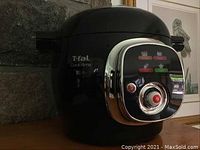Front view of T-fal Cook4me showing glossy black finish and chrome accented control panel with power button and dial.
