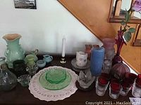 Overview of vintage glass collection on table including green dishes, multiple colored vases, candle holders, and decorative pieces.