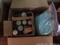 View of the box showing a large bag of blue wax pellets and six candles in glass jars packed in a cardboard divider.