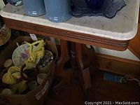 Side view of wooden table with white marble top and carved wooden base.