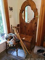 Photo of pine hall bench with ornate mirror and hooks, bench storage compartment closed, walking sticks leaning against the chair and bench.