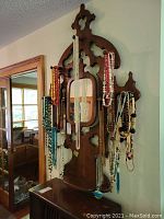 Front view of wooden wall rack with multiple assorted beaded necklaces hanging, showing variety and colors.