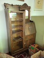 Photo showing full front view of wood cabinet with glass door bookcase (damaged glass) and secretary desk with mirror and drop-down desk section.