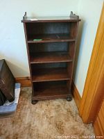 Front view of wooden 4-shelf bookcase showing four shelves with some scratches on surfaces and a classic raised side panel design on top.