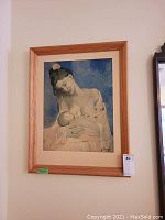 Full view of framed Picasso print showing mother breastfeeding baby with wooden frame on beige wall.
