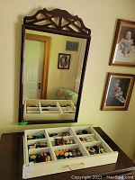 Wood framed mirror hanging on wall above table with white jewelry tray containing earrings, brooches, and hair jewelry.