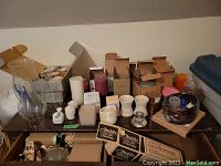 Wide shot of table holding various candles, candle holders, boxed items, and hurricane shades.