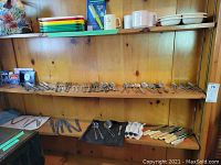 Full view of wooden shelves with assorted silver plate cutlery including forks, knives with cream handles, and spoons arranged in rows.