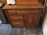 Front view of a wooden cabinet showing two drawers and one door with wooden handles and knob.