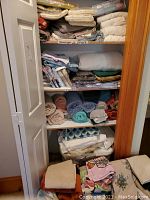 Closet shelves filled with neatly folded bed sheets, pillowcases, and towels in various colors and fabric types.