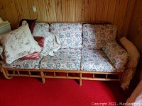 Photo of rattan sofa with floral cushions and extra pillows, showing front view and condition of cushions and frame.