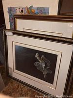 Overview photo of the three framed art prints grouped together in storage, showing one owl print with black background and dark frame, and other prints behind it.