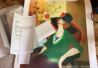 Photo showing the signed art print on carpet with additional paperwork including Certificate of Authenticity.