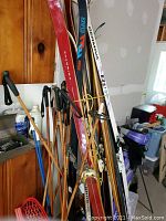 Assorted skis, poles and a red plastic snowshoe leaning against a cabinet