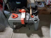 Router mounted on a plastic stand/table with an orange safety guard, guide fence with attached wood, and measuring scales visible