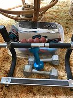 Assorted workout weights including small dumbbells, a handheld massage roller, and components of a pull-up bar with foam handles.