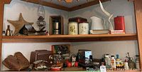 View of two shelves with assorted vintage decor and collectibles including leather boots, old radios, pitchers, tins, and decorative items.