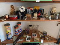 Two wooden shelves filled with various vintage collectibles including jars with artifacts, tins, bottles, figurines, and camera accessories