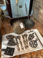 Wide view showing entire collection of assorted ironware including small iron, utensils, trivets, cauldron, poker, and rod.