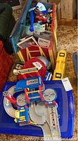Photo displaying assortment of toys in and around a red toy chest, including a Service Center playset, fire helmet, yellow toy truck, and action figures.