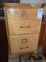 Front view of wooden filing cabinet showing two drawers with metal handles, top drawer locked with key, and wood grain finish.