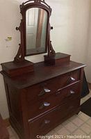 Front view of dark wooden vintage dresser with attached mirror, three drawers with carved handles, and two small raised compartments on top surface beside the mirror.
