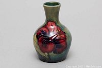 Front view of Moorcroft bud vase showing red flower design on green background glaze with crazing