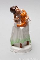 Front view of the porcelain figurine showing the girl and teddy bear on a table with white and green cloth, mounted on crackled base.