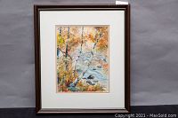 Framed watercolour painting showing a nature scene with autumn foliage and river, surrounded by white mat and dark wood frame.