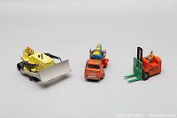 Three vintage die-cast metal toy construction vehicles positioned side by side: yellow bulldozer, orange cement mixer, and orange forklift.